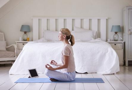 Woman meditating by bed with tablet