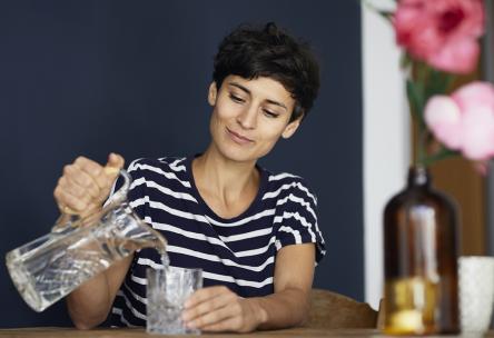 Woman at home sitting at wooden table pouring water into glass