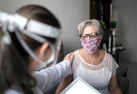Senior patient woman being comforted by doctor, both wearing masks.