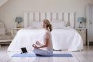 Woman meditating by bed with tablet