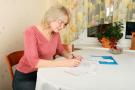 Photo: Woman sitting at home dining table, writing a list